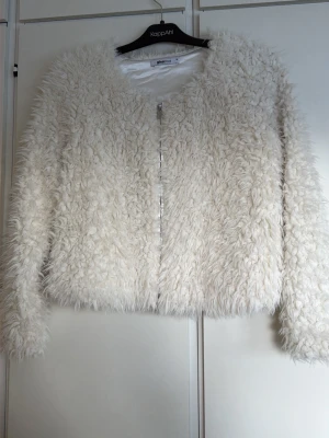 Vit fluffig fejkpäls Gina Tricot XS - Supersnygg vit fejkpäls från Gina Tricot i storlek XS. Jackan är fluffig och har långärmad design med dragkedja framtill. Perfekt för dig som vill ha en mysig och trendig look. Fodrad insida i glansigt material.