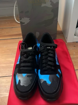 Valentino Garavani Rockrunner blå/svarta - Säljer ett par Valentino Garavani Rockrunner sneakers i svart och blått med camouflagemönster. Skorna har svarta snören, detaljer i mocka och skinn samt den ikoniska nitar på hälen. Snygg och chunky sula för extra attityd. Hör av er vid frågor✅
