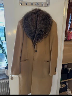 Tiger of Sweden rock / kappa med exklusiv naturpäls - Säljer en helt oanvänd klassisk rock från Tiger of Sweden, i elegant kamelfärg. Storlek Medium. Rocken är i högkvalitativ ullblandning (nypris ca 6 000 kr utan päls). Kragen är i naturlig päls (räv) och har monterats professionellt av en pälsbutik på Drottninggatan. Bara pälsen och monteringen gick på ca 6 000 kr. Totalt nypris alltså 12 000 kr. Rocken är oanvänd, helt i nyskick. En tidlös och lyxig ytterrock med det lilla extra – perfekt för dig som vill ha något unikt och elegant.  Strl 48 Fun
