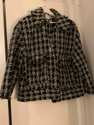 Svartvit rutig kavajjacka - Säljer en svartvit kavajjacka med rutigt mönster och grov struktur. Jackan har krage, raka ärmar och fransiga kanter. Från H&M 