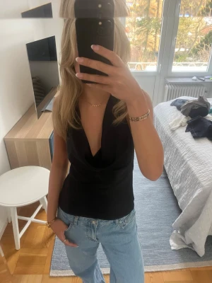 Svart halterneck topp i satin - Säljer en svart halterneck topp i satin med knyt i halsen och öppen rygg. Perfekt att styla med jeans eller kjol till en utekväll eller middag!