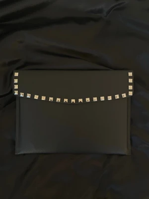 Datorfodral med silver nitar i läder imitation  - Rea - endast 199 kr (ord. pris 249 kr)! Stilrent datorfodral tillverkat av veganskt läder i vattentätt material. Fodralet stängs med knapp. Fodralet skyddar din dator effektivt samtidigt som det ger din outfit en extra touch. ⚜️ Storlek: 34 × 25 cm – passar svarta HP Chromebooks och andra datorer i liknande storlek. 1-3 arbetsdagar leverans 📦 