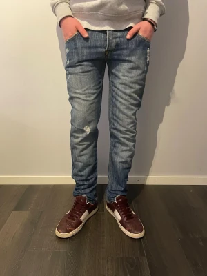 Nudie Jeans Regular Ralf blå jeans - Säljer ett par Nudie Jeans Regular Ralf i klassisk blå tvätt med slitningar och broderade detaljer på bakfickorna. Jeansen har normal passform, raka ben och är tillverkade i bomull. Snygga slitningar framtill och på sidorna för en avslappnad look. Lägg gärna prisförslag 