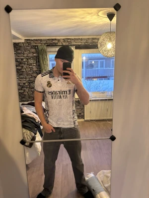 Real Madrid x Y-3 vit matchtröja - Säljer en Real Madrid x Y-3 matchtröja från Adidas. Tröjan är vit med svart och guld detaljer, har korta ärmar och ett unikt mönster över hela tyget. Klassisk krage med knäppning och broderad klubbmärke på bröstet. Perfekt för fotbollsfans!