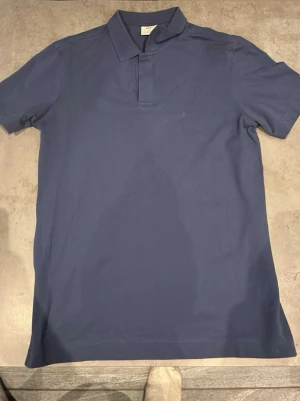 Marinblå pikétröja från MNG - Säljer en stilren marinblå pikétröja från MNG i slim fit. Tröjan har klassisk krage, korta ärmar och knäppning framtill. Tillverkad i mjuk bomull som känns skön mot huden. Perfekt till jeans eller shorts för en clean look.aldrig använt 