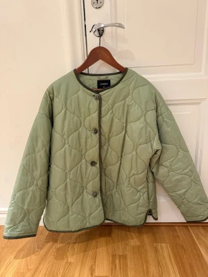 Quiltad grön jacka från Lindex - Snygg quiltad jacka i ljusgrönt från Lindex. Jackan har rund halsringning, knäppning med knappar framtill och mörkare kantband. Lätt oversized passform och långa ärmar. Perfekt för lager på lager under höst och vår.