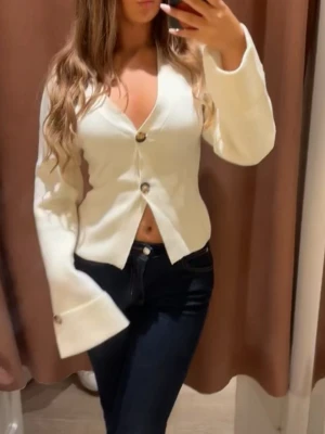 Vit kofta med vida ärmar och knappar - Säljer en stilren vit kofta med v-ringning och stora dekorativa knappar framtill. Koftan har vida, långa ärmar och är något croppad vilket ger en trendig look. 