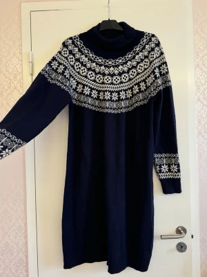 Stickad klänning med nordiskt mönster – mörkblå från Lindex - Produktbeskrivning: En mörkblå stickad klänning. Köpt från Lindex ett par år sedan. Använd bara ett fåtal gånger. Storlek står inte på plagget men den passar perfekt för mig med S/M i storlek. Har oversized passform. Bröstmått: ca 120cm (60cm x 2). Längd: ca 106cm. Med klassiskt nordiskt/norskt mönster upptill och på ärmarna.  Ett perfekt plagg för höst och vinter – varmt, bekvämt och tidlöst. Mjuk stickad kvalitet Passar lika bra till vardag, jobb och vintermys.  En riktig garderobsklassiker fö