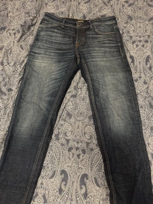 Tapered blå jeans Tapered Mike - Säljer ett par snygga blå jeans i modellen Tapered Mike. Jeansen har en tvättad look med ljusare partier och klassiska fem fickor. Passformen är tapered vilket ger en modern siluett. Perfekta till sneakers eller boots.