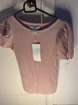 Beige,rosa stickad topp med puffärm  - Säljer en beige stickad topp från Aéryne med puffiga korta ärmar och rund hals. Toppen har ett snyggt ribbat mönster och är gjord i mjukt material som känns skönt mot huden. Perfekt att styla med jeans eller kjol för en cool look.