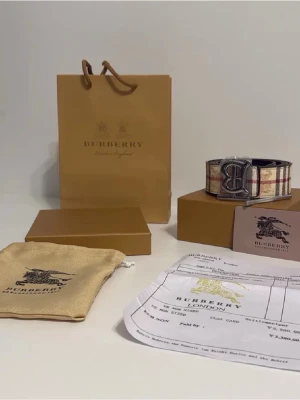 Rutig Bur berry bälte/skärp i skinn - Säljer en ikonisk skärp från  med klassiskt rutigt mönster i beige, svart och rött. Skärpet har en stilren passform och är tillverkad i exklusivt skinn. Perfekt för dig som vill sticka ut med en tidlös och lyxig look.