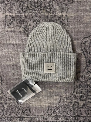  stickad mössa Acne Studios - Säljer en grå ribbstickad mössa från Acne Studios med det ikoniska ansiktslogotypen framtill. Mössan är tillverkad i 100% ull och har en bred uppvikt kant för extra stilpoäng. Perfekt accessoar för kyliga dagar.