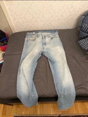 Levi's 501 ljusblå jeans 33/32 - Klassiska Levi's 501 jeans i ljusblå tvätt med raka ben och normal passform. Jeansen har fem fickor, knappgylf och den ikoniska röda Levi's-lappen på bakfickan. Tillverkade i slitstarkt bomullsjeansmaterial, perfekta för en avslappnad look.
