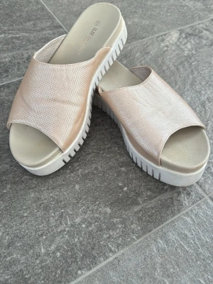 Beige sandaler från Ilse Jacobsen - Säljer ett par snygga sandaler från Ilse Jacobsen i beige med lätt glansig finish. De har öppen tå, bred rem över foten och vit, räfflad platåsula. Perfekta för sommardagar och riktigt bekväma att gå i.