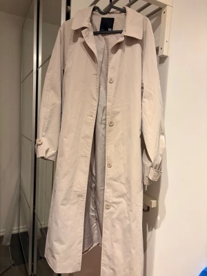 Beige trenchcoat med bälte - En beige trenchcoat från Lager 157. Jackan har knappar framtill och bälte i midjan. 