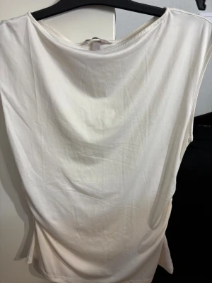 Vit ärmlös linnetopp från H&M - Säljer en enkel och stilren vit linnetopp från H&M i storlek M. Toppen har en lös passform, breda axelband och rundad halsringning. Materialet är mjukt och svalt, perfekt för varma dagar eller som layering-plagg.