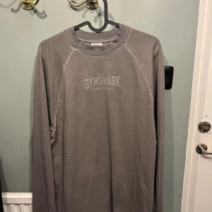 Grå/ beige oversized tröja från Gymshark - Säljer en grå långärmad tröja från Gymshark i storlek XS. Tröjan har rund halsringning och tryckt logga framtill. Perfekt för träning eller chill, tillverkad i mjuk bomullsmix för skön känsla. Oversized så passar folk i S som M lika bra 