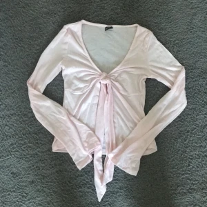 Ljusrosa omlottopp från Gina Tricot - Supersöt ljusrosa omlottopp från Gina Tricot i tunn bomullsmix. Toppen har långa ärmar, djup v-ringning och knyt framtill som ger en snygg detalj. Perfekt att styla med jeans eller kjol för en trendig look. Använd 1-2 ggr, nypris: 300kr