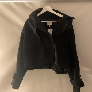 Svart kappa från H&M - Helt ny kappa med trenchcoat aktig stil. Nypris 449kr. Varm och perfekt till höst/vinter. Pris kan diskuteras 💕