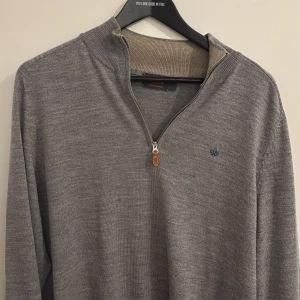 Grå merinoulltröja från Morris - Snygg grå långärmad tröja från Morris i 100% merinoull. Tröjan har en stilren half zip-dragkedja med läderdetalj och diskret broderad logga på bröstet. Perfekt för dig som gillar klassisk och clean stil. Storlek XL men passar mer L enligt mig.