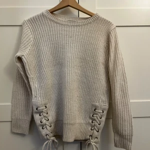 Beige stickad tröja med snörning - Superfin beige stickad tröja från New Look Petite med cool snörningsdetalj i sidorna nertill. Tröjan har lång ärm, rund halsringning och grovstickad struktur som ger en mysig vibe. Perfekt för lager på lager under höst och vinter.
