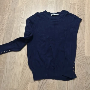Mörkblå långärmad tröja från Zara - Mörkblå långärmad tröja från Zara med rund halsringning och dekorativa knappar längs ena ärmen och nederkanten. Tunn och mjuk, perfekt för lager-på-lager. Enkel och stilren design som passar till det mesta.