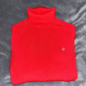 Röd polotröja med broderad Morris logga - Ribbstickad röd polotröja med lång ärm och hög krage från märket Morris. Tröjan har en liten broderad Morris logga på bröstet. Perfekt för dig som vill ha en klassisk men ändå snygg look med lite extra edge. Använts enstaka gånger och är som helt ny! Originalpris från Morris butik: 1500kr