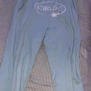 Ljusblå mjukisbyxor från Starlight - Ljusblå mjukisbyxor från Starlight med resår i midjan och vit logga framtill. Byxorna har en avslappnad passform och är tillverkade i mjukt bomullsmaterial. Perfekta för chill dagar eller när du vill vara bekväm men ändå se snygg ut. (Ny pris 799kr) 