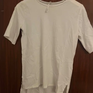 Vit t-shirt från 157, storlek S - Vit t-shirt från 157 i storlek S. Modellen har rund hals, korta ärmar och är tillverkad i mjuk bomull. T-shirten har en enkel och clean look med slits i nederkanten på sidorna. Perfekt för dig som gillar minimalistisk stil.