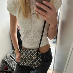 Svart och vit väska från Malene Birger - Snygg axelväska från Malene Birger i svart och vit med grafiskt mönster och guldfärgad logga framtill. Väskan är i präglat skinn och har justerbar axelrem. Perfekt storlek för det viktigaste och ger en cool touch till din outfit. Några få defekter. 