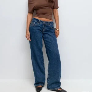 Blåa wide jeans med låg midja - Säljer ett par blåa jeans med låg midja och breda ben. Jeansen har klassiska fickor fram och bak, kontrastsömmar och en avslappnad passform. Perfekta för dig som gillar en loose och trendig stil.