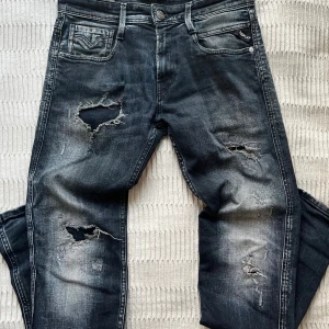 Replay Anbass blåa - Säljer ett par mörkblå Replay Anbass jeans med slitningar. Jeansen har klassisk femficksdesign, tydlig tvättad look och logga på fickan. Materialet är jeans och passformen är slim fit. Storlek 28/32.