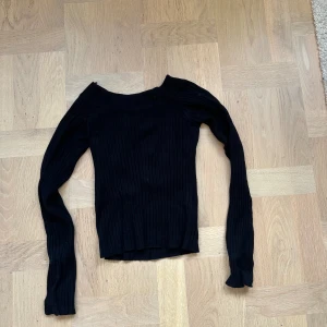 Svart ribbad tröja Gina Tricot  - Svart ribbad långärmad tröja från Gina Tricot i storlek XS. Tröjan har en tight passform och är tillverkad i ett stickat material med bred halsringning. Perfekt att styla med jeans eller kjol för en clean look.
