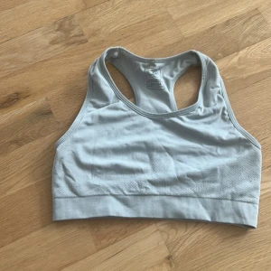 Ljusgrå sporttopp från H&M - Sportig ljusgrå topp från H&M med brottarrygg och bred resår nedtill. Tillverkad i mjukt och stretchigt material som passar perfekt för träning. Enkel och stilren design utan mönster, med diskret struktur på sidorna.