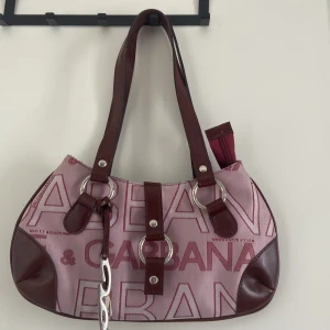Rosa Dolce & Gabbana handväska - Vintage dolce & gabbana väska i rosa och mörkröd/brun färg. Nästan aldrig använd. Den går även inte att få tag i längre eftersom den är gammal! Jag har sett liknande väskor för över 5000kr men jag säljer billigare!! 