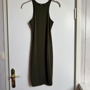 Grön tight klänning Bik Bok - Säljer en mörkgrön, tight och ärmlös klänning från Bik Bok. Klänningen har en rak, kroppsnära passform och är tillverkad i mjuk bomull med lite stretch. Modellen är enkel och stilren med hög hals och racerback-rygg. Perfekt för dig som gillar minimalistisk stil.