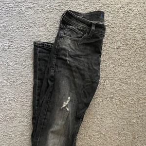 Svarta Slim Glenn jeans med slitningar - Svarta jeans från Slim Glenn med snygga slitningar och tvättad look. (Hålet vid knät är lappat) Modellen har en smal passform i storlek 29/32. Dom har inga defekter då jag har använt dom en gång. Jeansen är tillverkade i bomull och har en modern, lite sliten stil som passar perfekt nu till hösten. Hör av er vid funderingar!