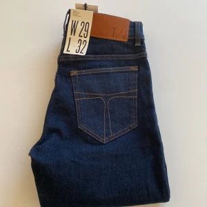 Tiger of Sweden mörkblå jeans W29 L32 - Mörkblå jeans från Tiger of Sweden med klassisk femficksdesign, kontrastsömmar och läderpatch bak. Modellen har midwaist och tapered ben, tillverkad i slitstarkt bomullsjeansmaterial. Snyggt och stilrent val för dig som gillar enkel och modern look. Aldrig använda 
