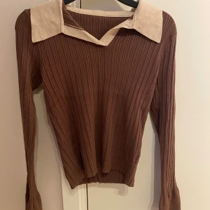 Brun ribbad långärmad tröja med krage från SHEIN  - Brun ribbstickad långärmad tröja med bred, ljusbeige krage och v-ringning. Tröjan har en slim passform och är tillverkad i ett stretchigt, stickat material. Ärmarna är mer öppna och stretchiga. Perfekt för dig som gillar retrovibbar och vill ha något unikt i garderoben.