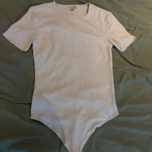 Vit kortärmad body - En enkel och stilren vit bod med korta ärmar och rund halsringning. Gjord i mjuk bomullsmix som sitter skönt mot kroppen. Perfekt att styla med jeans eller kjol för en clean look.