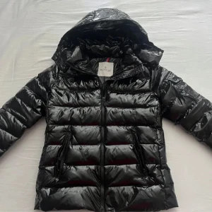 Moncler jacka - Säljer en svart pufferjacka från Moncler med glansig finish och klassisk logga på ärmen. Dustbag finns