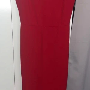 Röd långklänning med volang och rosett - Snygg röd långklänning med djup v-ringning och markerad midja. Klänningen har en stor rosett baktill och volangdetaljer som faller längs kjolen. Perfekt för dig som vill sticka ut med en elegant och trendig look.