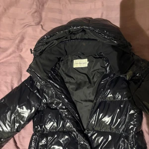 Svart pufferjacka från Calvin Klein Jeans - Snygg svart pufferjacka från Calvin Klein Jeans med glansig finish och Jackan 