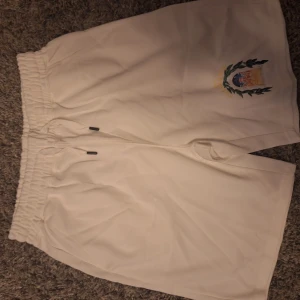Vita shorts från Casablanca Tennis Club - Snygga vita shorts från Casablanca Tennis Club med broderad logga och motiv på ena benet. De har elastisk midja med snörning för skön passform. Perfekta för tennis eller chill dagar. Materialet känns mjukt och svalt.
