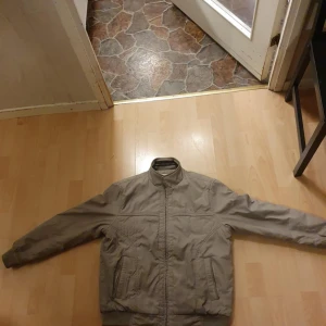 Beige bomberjacka från Chunlih, M - Säljer en beige bomberjacka från Chunlih i storlek M. Jackan har en klassisk bombermodell med dragkedja framtill, ribbade muddar och två fickor. Insidan är fodrad med mjuk, mörkgrå teddy för extra värme. Perfekt för dig som vill ha en stilren och bekväm jacka.