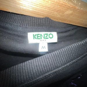 Svart Kenzo sweatshirt med tigertryck - Svart sweatshirt från Kenzo med ikoniskt broderat tigerhuvud i lila, rosa och blå toner på bröstet. Tröjan har rund halsringning och långa ärmar. Perfekt statement-plagg för dig som vill sticka ut med cool design och färgstarka detaljer.