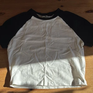 Svartvit t-shirt från H&M Divided - Säljer en svartvit t-shirt från H&M Divided i storlek M. Magtröja. Klassisk basebollmodell med svarta ärmar och vit kropp. 
