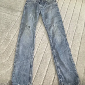 Crocker ljusblå slitna jeans 27/32 - Säljer ett par ljusblå jeans från Crocker i modellen 308 Tapered. Jeansen har flera slitningar och hål på benen för en cool, avslappnad look. Klassisk femficksdesign och rak passform. Perfekt för dig som gillar streetstyle.