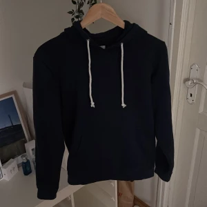 Mörkblå hoodie från Pier One med snörning - Svart hoodie från Pier One med vita snören i huvan och klassisk känguruficka framtill. Tröjan är tillverkad i mjuk bomullsmix och har lång ärm. Perfekt för chill dagar eller när du vill ha en enkel och stilren look.