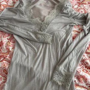 Grå långärmad topp med spets från Intimissimi - Supersnygg grå långärmad topp från Intimissimi i ultralätt material med kashmir. Djup v-ringning. Tröjan är i andvänd skick därav priser 
